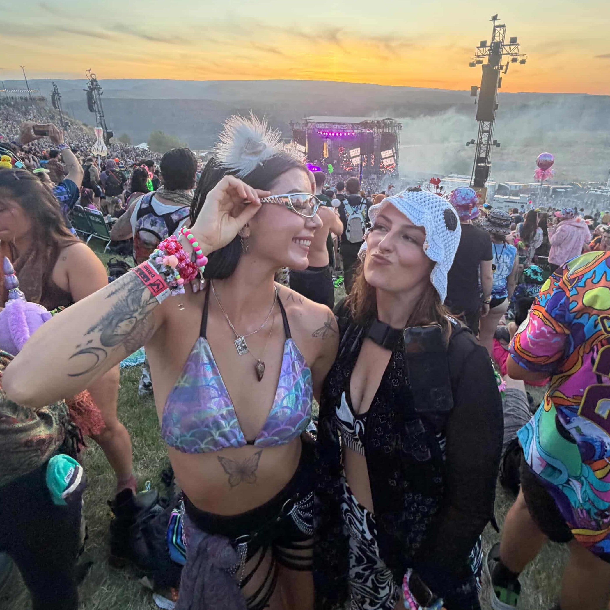 Two people at a music festival with a sunset over the ocean in the background.